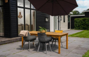Buiten eetgedeelte bij glamping met houten tafel, stoelen, grote parasol en uitzicht op modern huisje.
