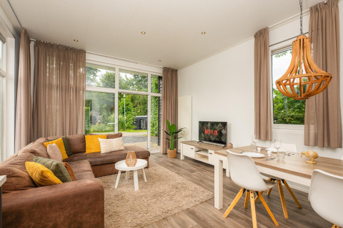 Glamping accommodatie met moderne zithoek, grote ramen, comfortabele bank en eettafel vlakbij de natuur.