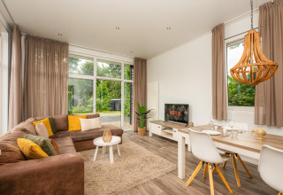 Modernes Glamping mit gemütlichem Wohnzimmer, großen Fenstern, Sofa und Essbereich in naturnaher Umgebung.