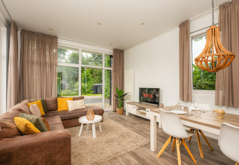 Stijlvolle glampingverblijf met moderne zithoek, grote ramen, zetel en eettafel dichtbij de natuur.