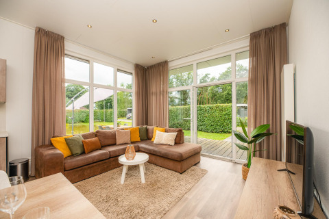 Cozy glamping living room with sectional sofa, large windows, sheer curtains and garden view outside.