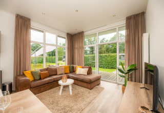 Cozy glamping living room with sectional sofa, large windows, sheer curtains and garden view outside.