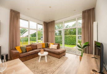 Cozy glamping living room with sectional sofa, large windows, sheer curtains and garden view outside.