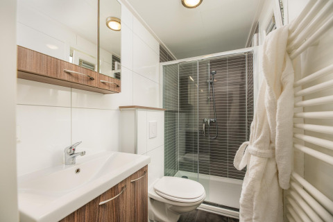 Modern badkamer in een glampingaccommodatie met douche, wastafel, toilet, houten kastjes en badjas.