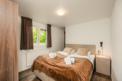 Knusse glamping slaapkamer met tweepersoonsbed, bruine gordijnen, nachtkastje en raam met uitzicht.