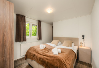 Et hyggeligt glampingværelse med dobbeltseng, brune gardiner, natbord og træmøbler.