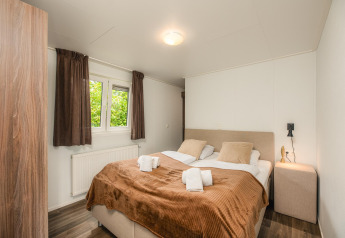 Knusse glamping slaapkamer met tweepersoonsbed, bruine gordijnen, nachtkastje en raam met uitzicht.