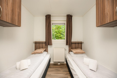 Lyst glampingværelse med to enkeltsenge, træmøbler, vindue med udsigt og rene håndklæder på sengen.