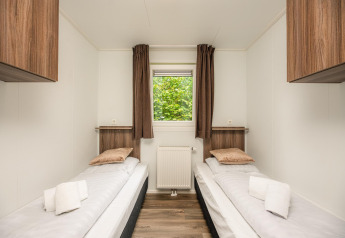 Stanza glamping luminosa con due letti singoli, mobili in legno, finestra panoramica e asciugamani puliti.