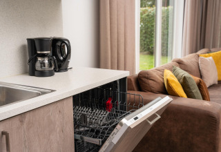 Alloggio glamping moderno con macchina da caffè, lavastoviglie aperta e divano con cuscini colorati vicino alle finestre.