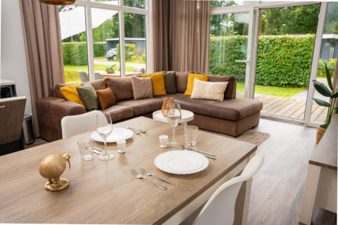 Moderne glamping-accommodatie met knusse zithoek, grote ramen en eettafel gedekt voor twee personen.