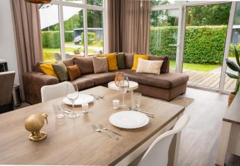 Modern glamping accommodation with cozy seating area, large windows, and a dining table for two people.