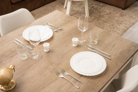 Table en bois dressée pour deux avec assiettes blanches, verres à vin et couverts dans un lieu glamping.