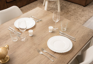 Wooden table set for two with white plates, wine glasses, and cutlery at a stylish glamping site.