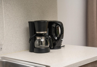 Sort kaffemaskine og elkedel på køkkenbord i glampingindkvartering med moderne indretning.
