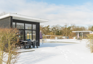 Forest lodge al Vakantiepark Hölte, Paesi Bassi, in inverno con neve, cabine moderne e tavolo all'aperto.