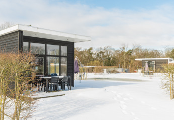 Forest lodge bij Vakantiepark Hölte, Nederland, in de sneeuw met moderne chalets en buitenzitjes.