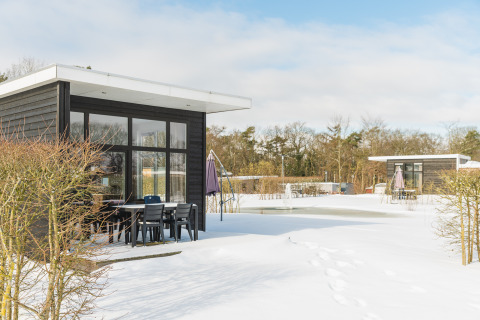 Forest lodge bij Vakantiepark Hölte, Nederland, in de sneeuw met moderne chalets en buitenzitjes.