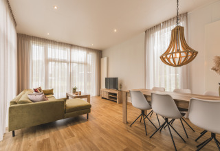 Lyst opholdsrum i Forest Lodge, Vakantiepark Hölte, Holland, med træmøbler og store vinduer.