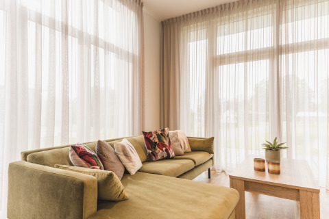 Helles Wohnzimmer in der Forest Lodge im Vakantiepark Hölte, Niederlande, mit Sofa und großen Fenstern.