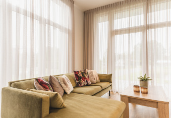 Bright, modern living room at Forest Lodge, Vakantiepark Hölte, Netherlands, with sofa and tall windows.