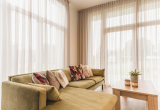 Helles Wohnzimmer in der Forest Lodge im Vakantiepark Hölte, Niederlande, mit Sofa und großen Fenstern.