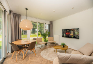 Soggiorno moderno presso Oak Lodge, Vakantiepark Hölte, Paesi Bassi, con Netflix sulla TV e ampie finestre.