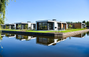 Moderne villaer ved vandet på Villa Nautica Lodge, omgivet af natur og spejlet i det rolige vand.