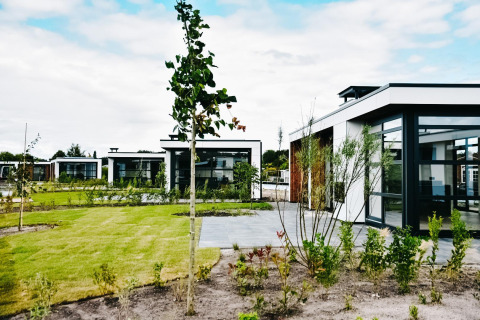 Cabañas modernas en Villa Nautica con grandes ventanales, césped verde y árboles jóvenes en el jardín.