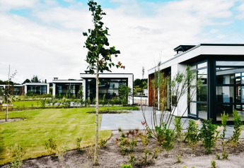 Cabañas modernas en Villa Nautica con grandes ventanales, césped verde y árboles jóvenes en el jardín.