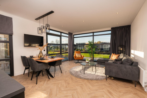 Modernes Wohnzimmer in der Villa Nautica Lodge mit großen Fenstern, Essbereich und gemütlichen Sofas.