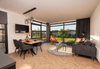 Moderne leefruimte in Villa Nautica met grote ramen, eetgedeelte en gezellige zithoek met tuinzicht.