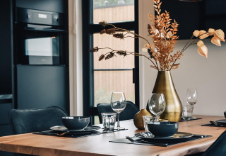Moderne eetruimte met houten tafel, zwarte stoelen en verlichting bij Villa Nautica, Nieuw Loosdrecht.