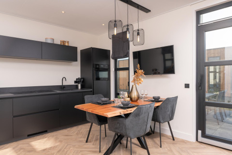 Moderne lodgekeuken en eethoek in Villa Nautica met zwart design, houten tafel en stijlvolle lampen.