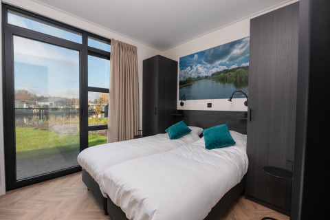 Modern lodge-slaapkamer met twee aparte bedden, grote ramen, uitzicht op natuur en groene kussens.