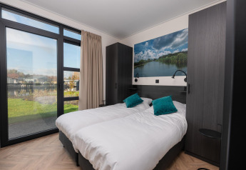 Moderne lodge-soveværelse med to enkeltsenge, store vinduer, naturudsigt og grønne pyntepuder.