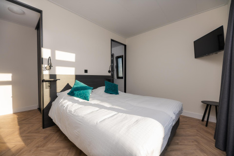 Helles Schlafzimmer in der Villa Nautica Lodge mit Doppelbett, zwei grünen Kissen und Wand-TV.
