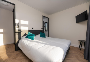 Lichte slaapkamer in Villa Nautica lodge met dubbel bed, twee groene kussens en een wand-tv.