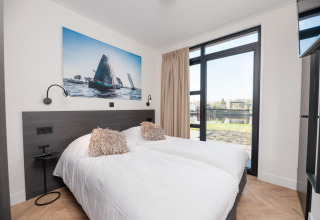Habitación luminosa y moderna en una cabaña con dos camas, gran ventana, vista al lago y arte de veleros.