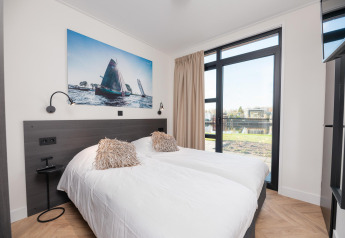 Habitación luminosa y moderna en una cabaña con dos camas, gran ventana, vista al lago y arte de veleros.