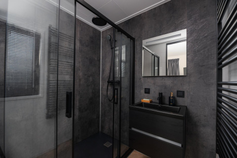 Baño moderno en un lodge con ducha negra, paredes oscuras, espejo cuadrado y tocador negro elegante.