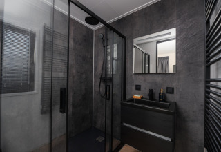 Baño moderno en un lodge con ducha negra, paredes oscuras, espejo cuadrado y tocador negro elegante.