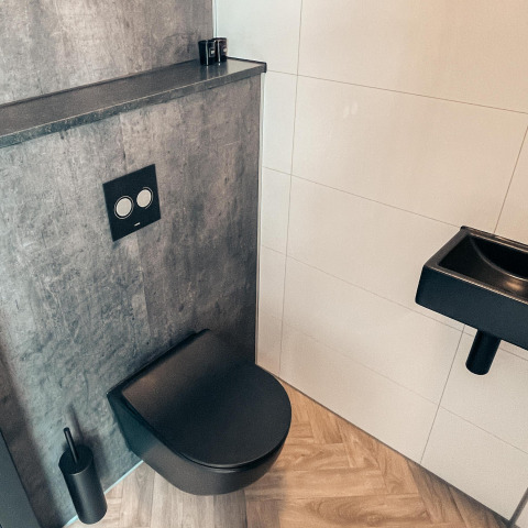 Moderne lodge-badkamer met zwart hangtoilet, grijze muur, zwarte wasbak en houten vloer.