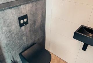 Moderne lodge-badkamer met zwart hangtoilet, grijze muur, zwarte wasbak en houten vloer.