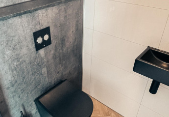 Moderne lodge-badkamer met zwart hangtoilet, grijs paneel, zwarte wasbak en houten vloer.