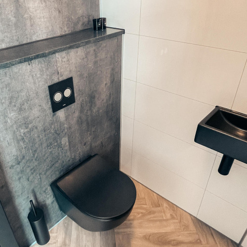 Baño moderno de lodge con inodoro negro mural, pared gris, lavabo negro y suelo de madera clara.