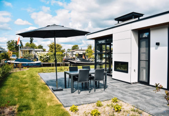 Casa moderna con terraza, muebles de jardín y sombrilla, ubicada tranquilamente junto al agua.