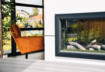 Intérieur du lodge Villa Nautica avec fauteuil orange, plante verte et cheminée moderne en plein jour.