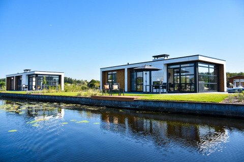 Lodges modernos de Villa Nautica con grandes ventanales y terrazas frente a un tranquilo canal bajo cielo azul.