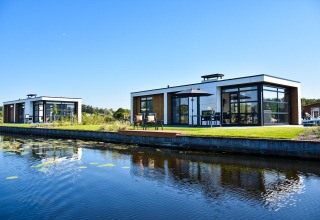 Lodges modernos de Villa Nautica con grandes ventanales y terrazas frente a un tranquilo canal bajo cielo azul.